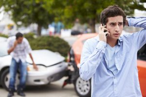 Upset teenage male making phone call after car accident